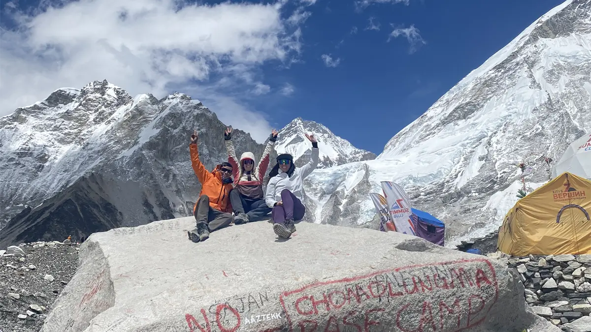 Trekkers sitting on the iconic stone marker at Everest Base Camp in Nepal