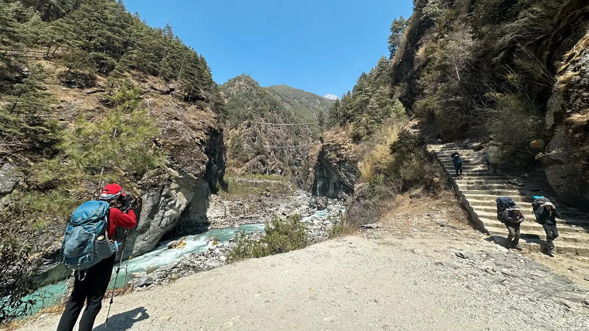 Trekkers walking toward Namche Bazaar with Hillary Bridge in the background